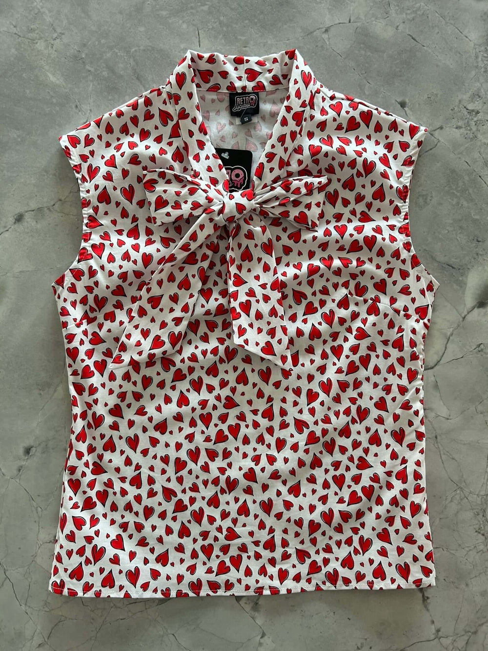 Vintage Style Tops This top is for the vintage lover at heart! Shown in our hearts print, this 100% cotton top features bust darts for a flattering silhouette, a side zippered closure for ease of wear, and an oversized bow at the neckline for that perfect 1950's inspired look. 