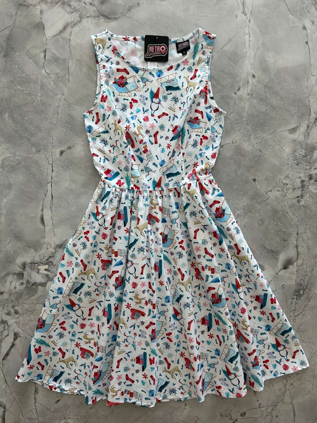 Introducing our Winter Cheer Vintage Dress. This dress boasts a fun and playful print featuring gnomes, sleds, ice skates, mittens, and reindeer. It&