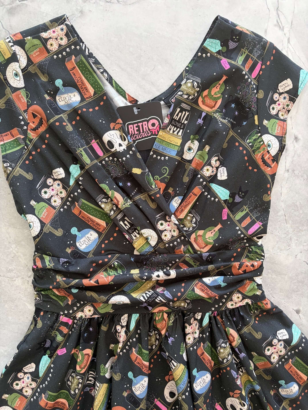 Made in USA, the Retrolicious Potions Greta dress is 100% cotton with a V-neck, gathered waist, pockets, and a true-to-size fit. Sizes XS–4X.